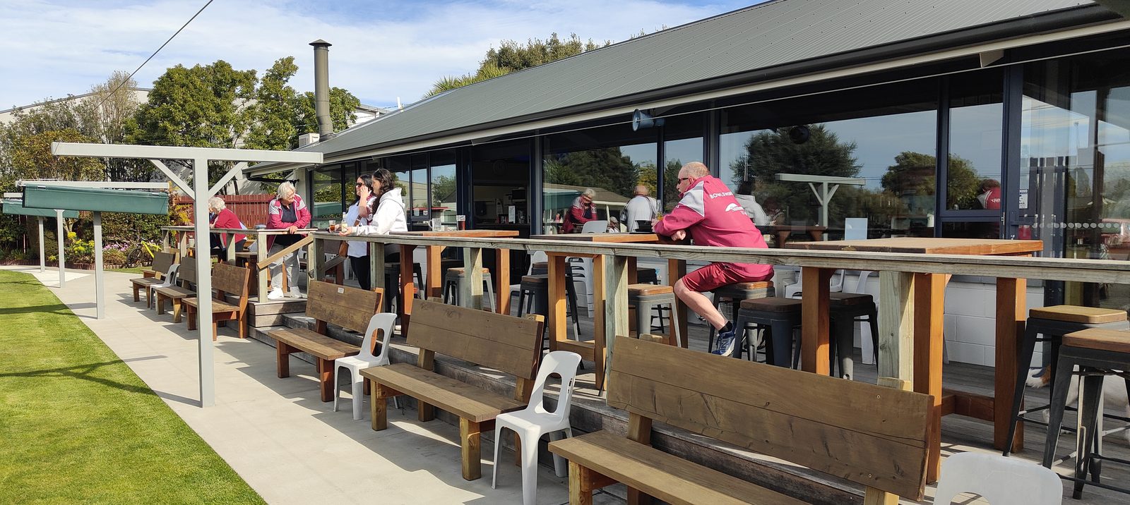 Members relaxing at tables on the Bowls Hornby clubhouse deck on a sunny afternoon.